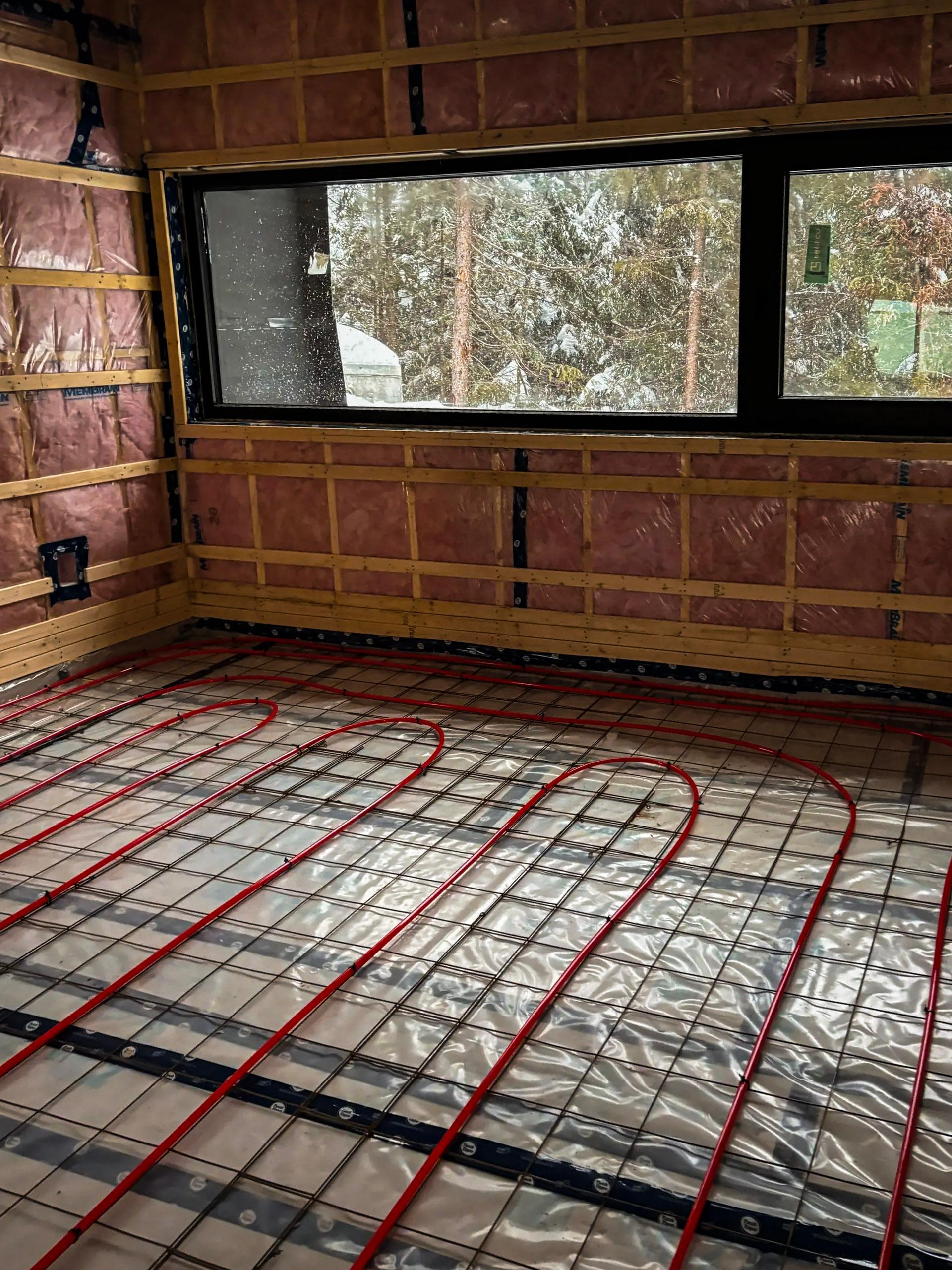 Système de chauffage au sol en cours d'installation dans une pièce en construction avec isolation et fenêtre panoramique.