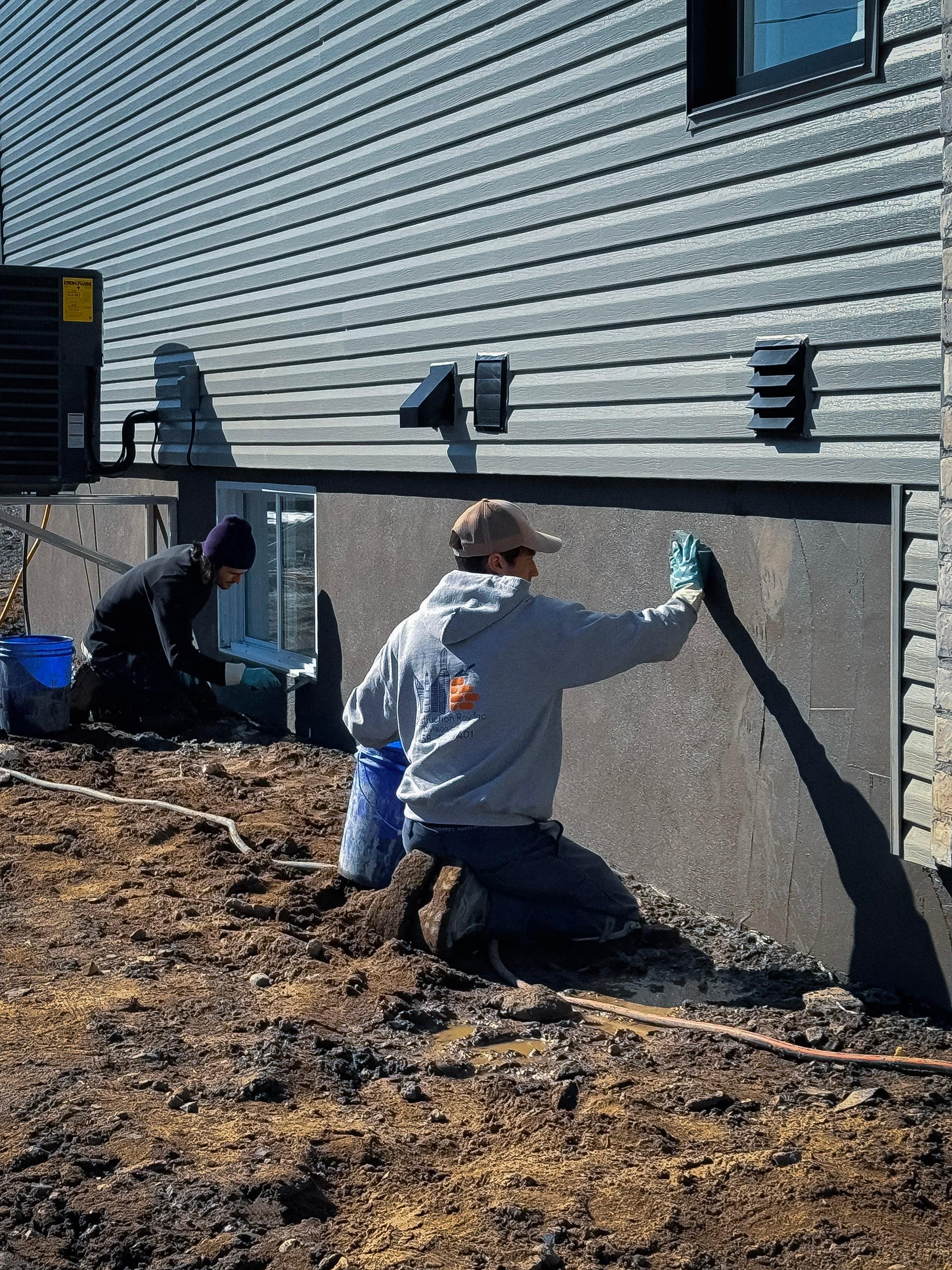 Travailleurs appliquant un revêtement sur une fondation de maison pour réparer des fissures et imperméabiliser