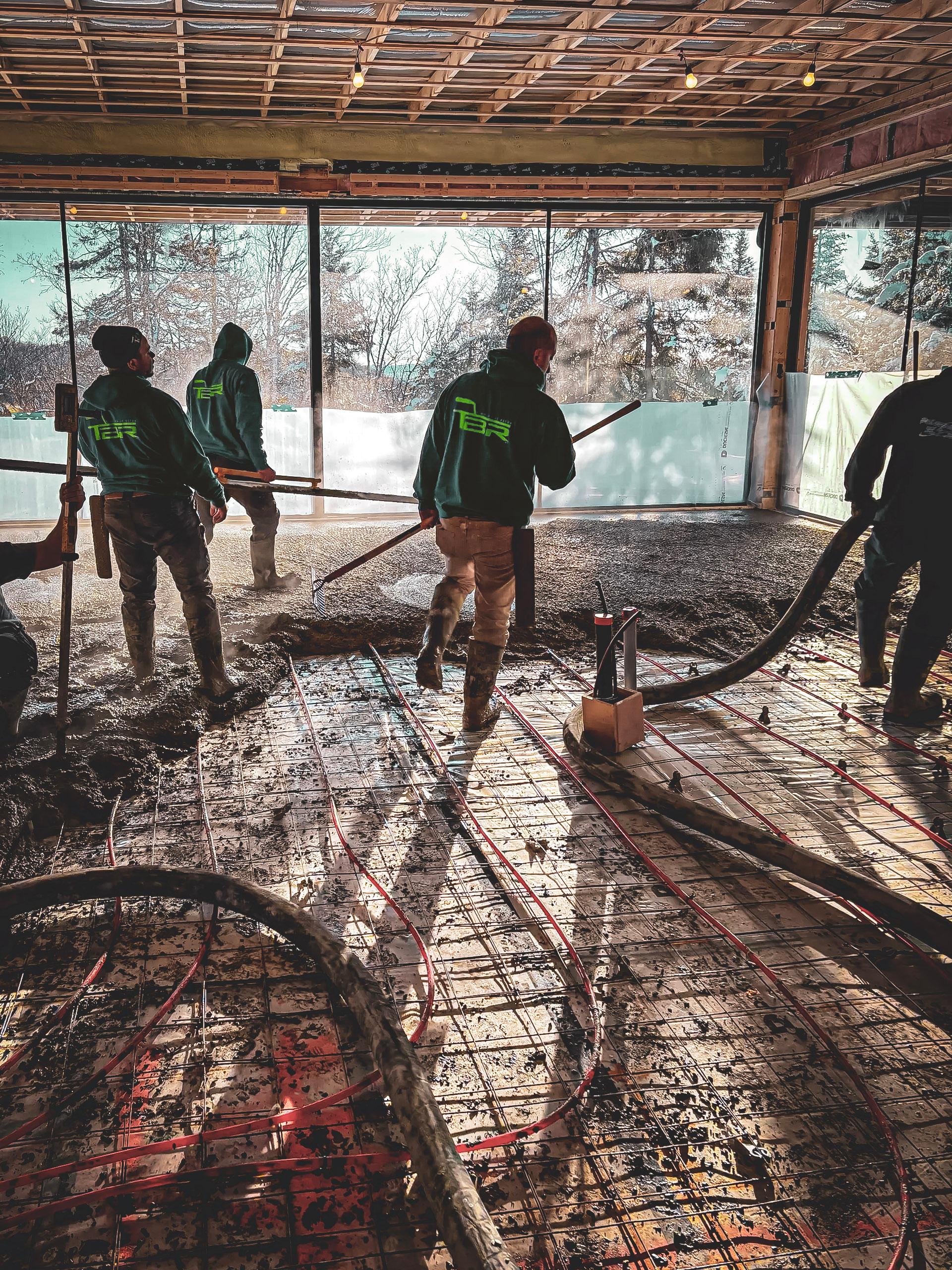 Travailleurs posant une dalle de béton dans un bâtiment en construction avec un système de chauffage au sol visible.