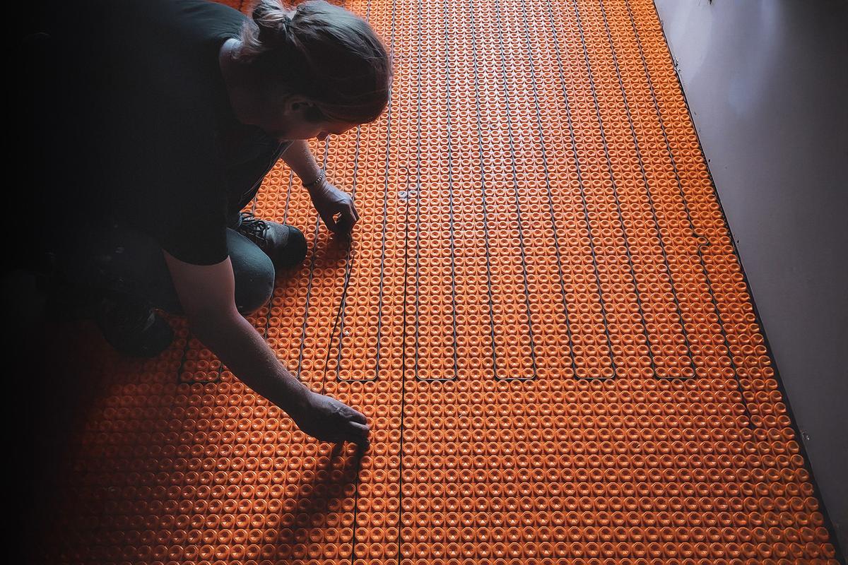Travailleur installant un système de chauffage au sol électrique avec une membrane orange dans une pièce en construction.